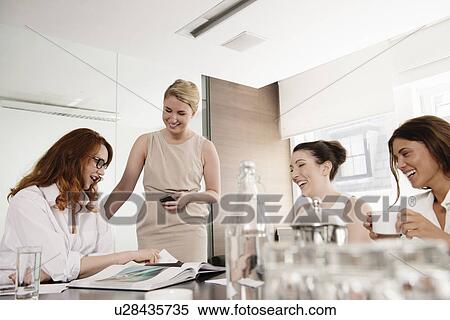 Stock Photography - Four businesswomen looking at portfolio in conference room. Fotosearch