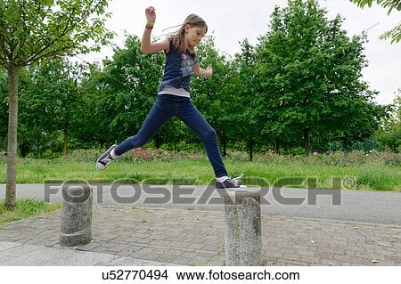 Picture - Girl jumping bollards mid air in park. Fotosearch