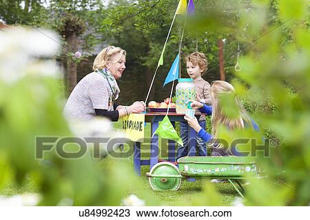 Stock Image - Grandmother buying lemonade from grandchildren's stand. Fotosearch