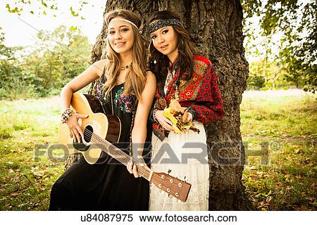 Stock Photography - Hippy girls by tree with guitar. Fotosearch