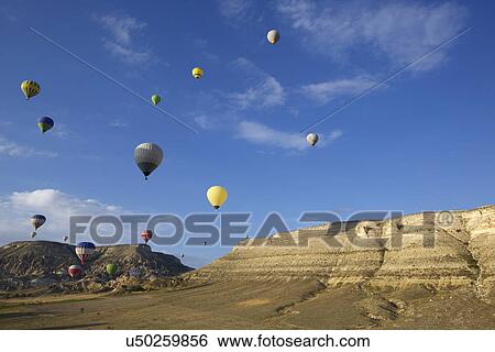 Stock Photograph - Large group of hot air balloons floating into distance over mountains, Cappadocia, Anatolia, Turkey. Fotosearch