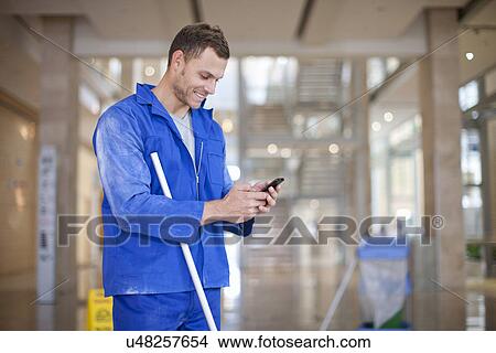 Male cleaner texting on smartphone in office atrium View Large Photo Image Picture - Male cleaner texting on smartphone in office atrium. Fotosearch