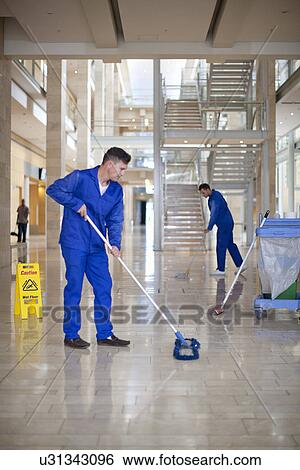Stock Photograph - Male cleaners mopping in office atrium. Fotosearch