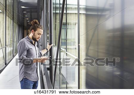 Stock Image - Man using smartphone in corridor. Fotosearch