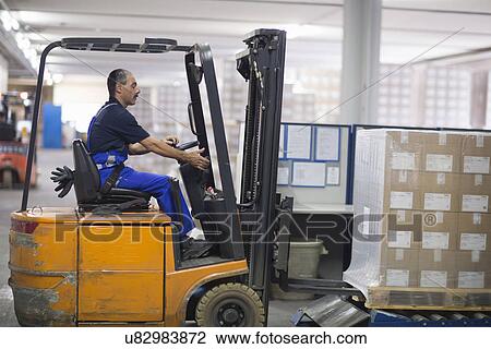 Stock Image - Mature man using forklift truck in factory. Fotosearch