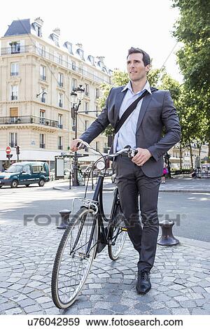 Stock Photo - Mid adult businessman pushing bicycle over cobbles, Paris, France. Fotosearch