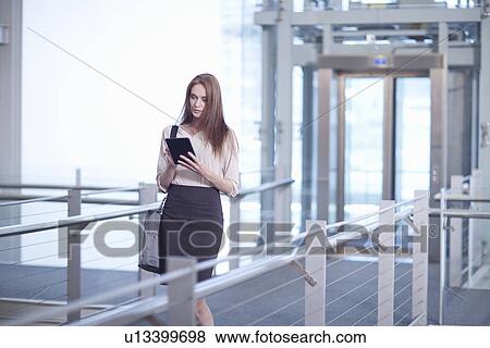 Stock Photo - Mid adult businesswoman using digital tablet on conference centre walkway. Fotosearch