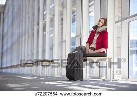 Picture - Mid adult businesswoman with wheeled case asleep in conference centre corridor. Fotosearch