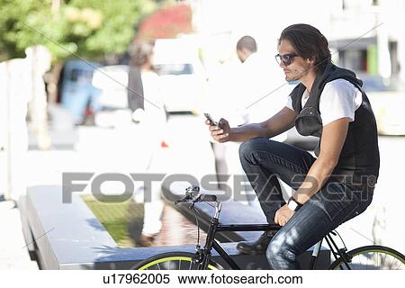 Mid adult male cyclist texting on smartphone on street View Large Photo Image Stock Photography - Mid adult male cyclist texting on smartphone on street. Fotosearch