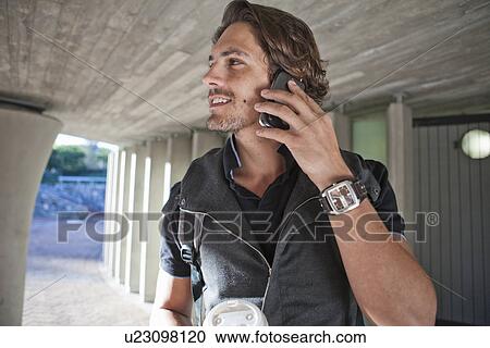 Stock Image - Mid adult man chatting on smartphone in city underpass. Fotosearch
