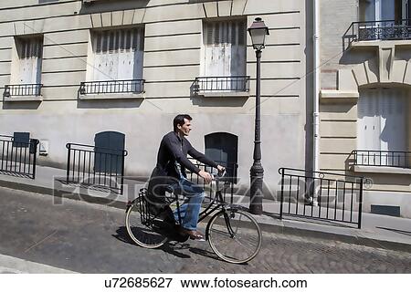 Mid adult man cycling down cobbled city street View Large Photo Image Stock Photo - Mid adult man cycling down cobbled city street. Fotosearch