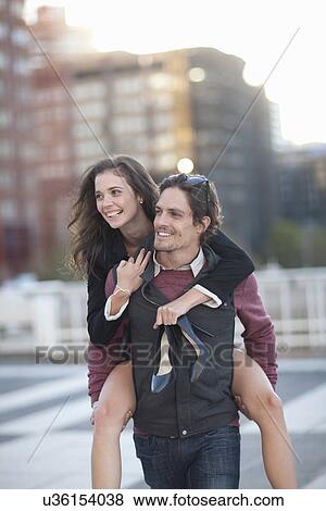 Mid adult man giving girlfriend piggyback in street View Large Photo Image Stock Photo - Mid adult man giving girlfriend piggyback in street. Fotosearch