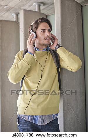 Stock Photo - Mid adult man listening to music on headphones in city underpass. Fotosearch