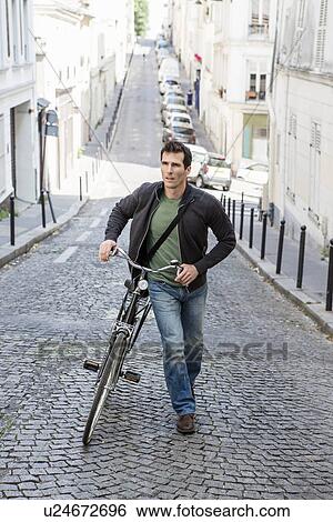 Mid adult man pushing bicycle up cobbled city street View Large Photo Image Stock Photograph - Mid adult man pushing bicycle up cobbled city street. Fotosearch
