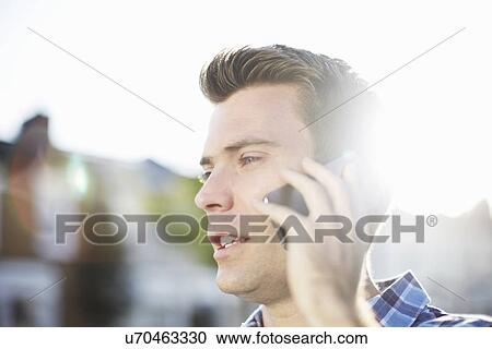 Stock Image - Mid adult man talking on smartphone on street. Fotosearch
