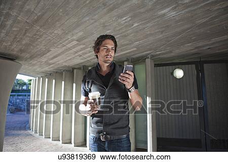 Stock Photo - Mid adult man texting on smartphone in city underpass. Fotosearch