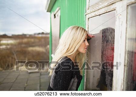 Stock Image - Mid adult woman peering into hut window. Fotosearch