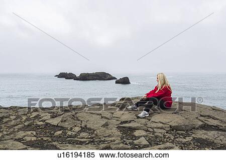 Stock Photography - Mid adult woman sitting on rocks, Dyrholaey, Iceland. Fotosearch