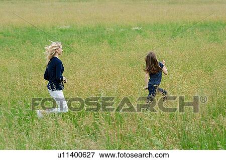 Stock Photo - Mother and daughter running through long grass field. Fotosearch