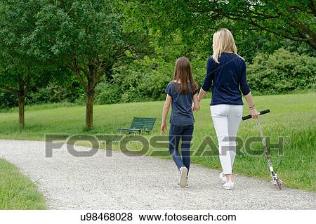 Stock Photo - Mother and daughter strolling in park with scooter. Fotosearch