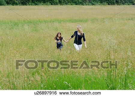 Stock Photograph - Mother and daughter strolling through long grass field. Fotosearch