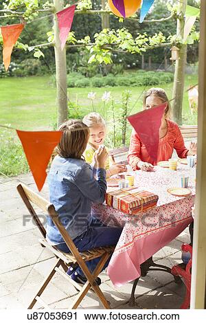 Stock Image - Mother chatting with children at patio table. Fotosearch