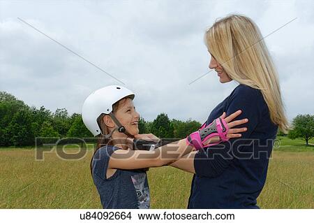 Picture - Mother fastening daughter's rollerblading helmet in park. Fotosearch