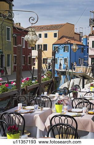 Stock Image - Multi colored houses and sidewalk restaurant, Burano, Venice, Veneto, Italy. Fotosearch