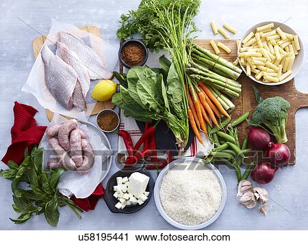 Stock Image - Overhead view of fish, pork sausage, feta and selection of fresh organic herbs and vegetable. Fotosearch