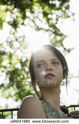 Stock Image - Portrait of serene young woman in park. Fotosearch