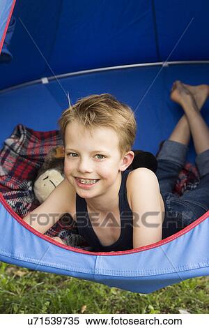 Stock Photography - Portrait of smiling boy lying in tent suspended above grass. Fotosearch