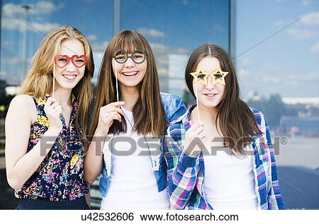 Stock Photograph - Portrait of three young women holding up spectacle costume masks. Fotosearch