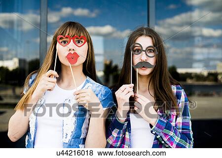 Stock Photo - Portrait of two young women holding up lip and eye costume masks. Fotosearch