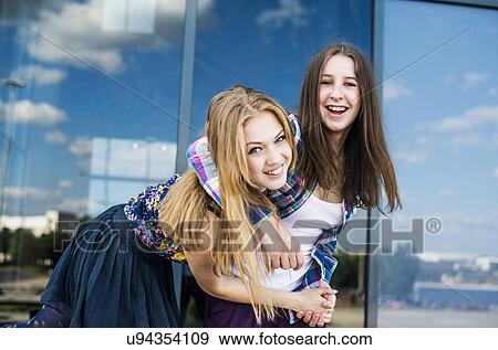 Stock Photo - Portrait of two young women with arms around each other in city. Fotosearch