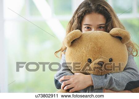 Stock Image - Portrait of young girl hugging teddy bear. Fotosearch