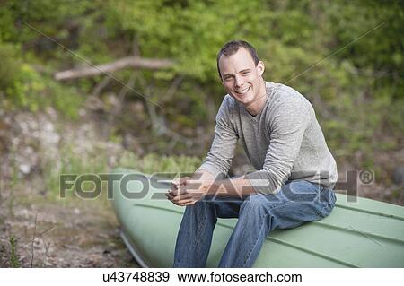 Portrait of young man sitting on upturned boat View Large Photo Image Stock Photo - Portrait of young man sitting on upturned boat. Fotosearch