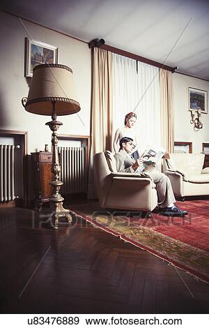 Stock Photo - Portrait of young vintage couple in sitting room reading newspaper. Fotosearch
