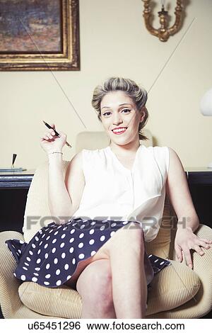 Stock Photograph - Portrait of young woman in armchair wearing vintage clothes. Fotosearch