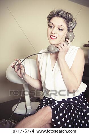 Picture - Portrait of young woman wearing vintage clothes and talking on vintage phone. Fotosearch