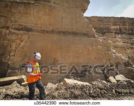 Stock Image - Quarry worker inspecting stone in quarry. Fotosearch