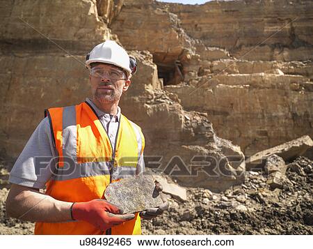 Stock Photography - Quarry worker inspecting stone in quarry, looking away. Fotosearch