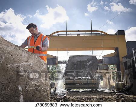Stock Image - Quarry worker measuring rock in front of stone saw. Fotosearch