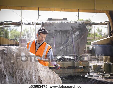 Stock Photography - Quarry worker measuring rock in front of stone saw. Fotosearch