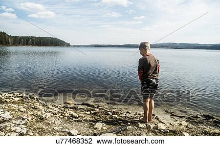 Stock Image - Rear view of boy standing on lakeside. Fotosearch