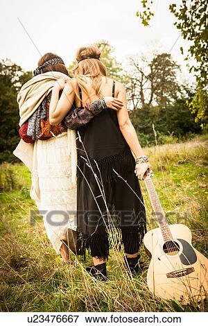 Stock Photo - Rear view of hippy girls walking through field with guitar. Fotosearch
