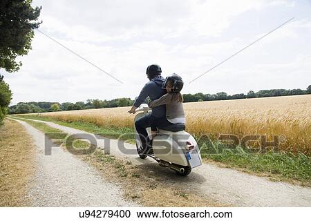 Rear view of mature man and daughter riding motor scooter along dirt track View Large Photo Image Stock Image - Rear view of mature man and daughter riding motor scooter along dirt track. Fotosearch