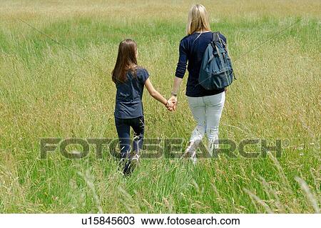Rear view of mother and daughter strolling through long grass field View Large Photo Image Stock Image - Rear view of mother and daughter strolling through long grass field. Fotosearch