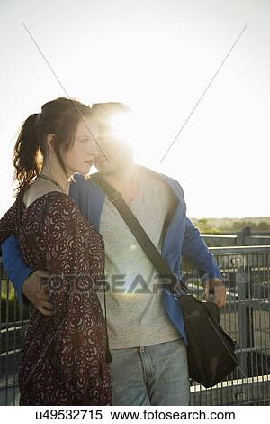 Stock Photography - Romantic young couple leaning against fence on rooftop. Fotosearch