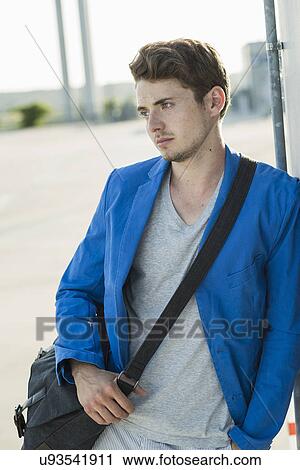 Stock Image - Serious young man leaning against wall. Fotosearch