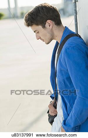 Serious young man with shoulder bag leaning against wall View Large Photo Image Stock Image - Serious young man with shoulder bag leaning against wall. Fotosearch